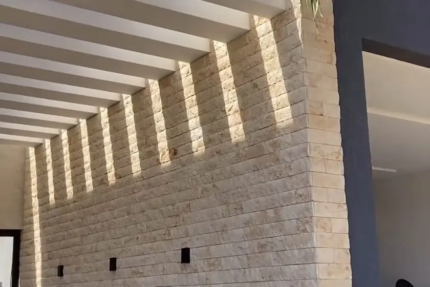 Parede revestida em régua cimentícia com iluminação rasante vinda de brises