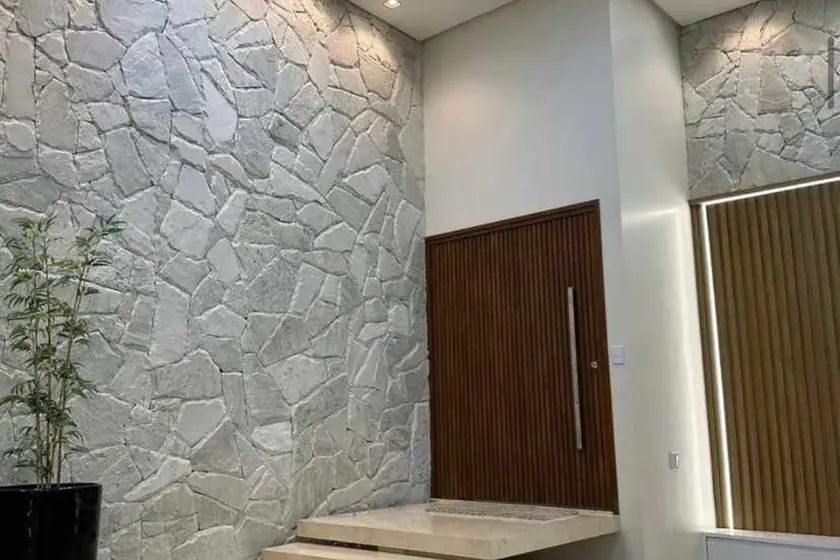 Hall de entrada com parede alta revestida em pedra natural clara e porta de madeira