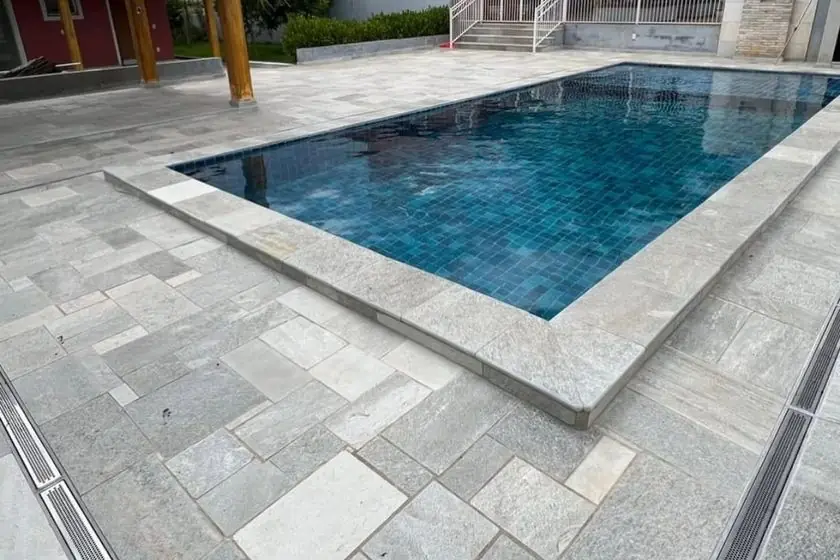 Borda de piscina revestida em pedra natural clara com deck ao redor